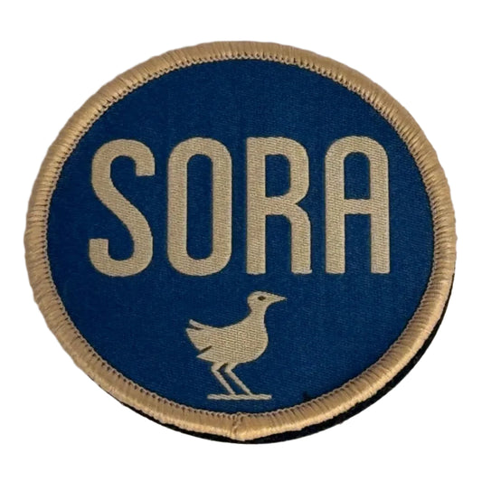 Round blue patch with 'SORA' text and a bird illustration on a gray background